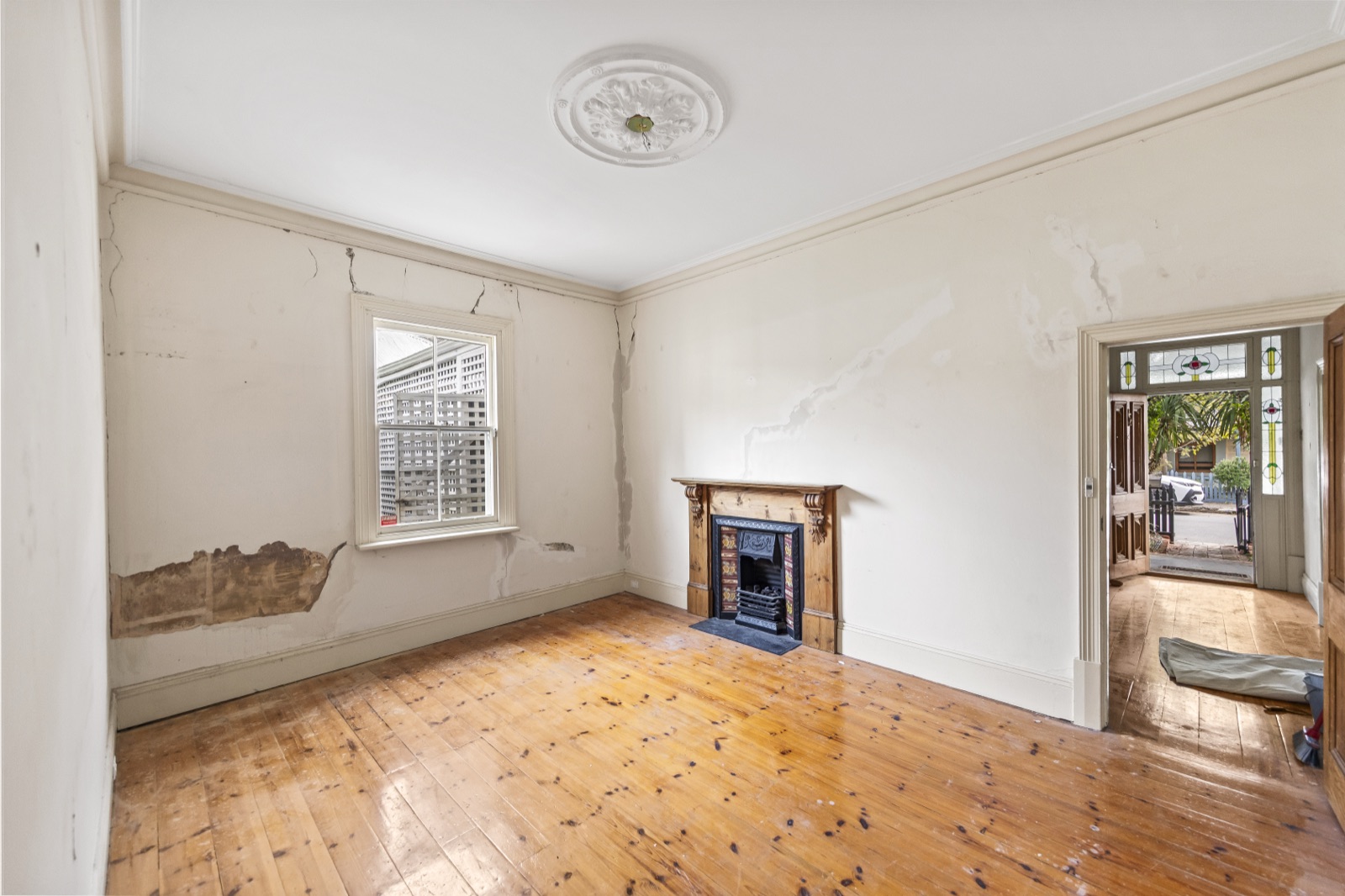 Front living room with cracked walls and bare floorboards before renovation